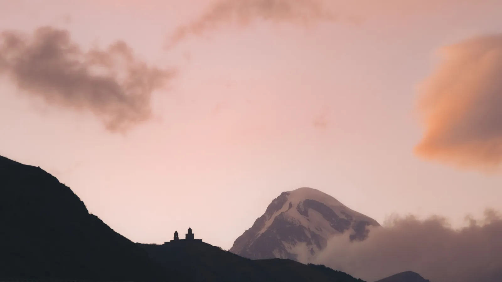 צללית כנסיית גרגטי על הרכס מול פסגת הר קזבק בגאורגיה בשמי דמדומים ורודים