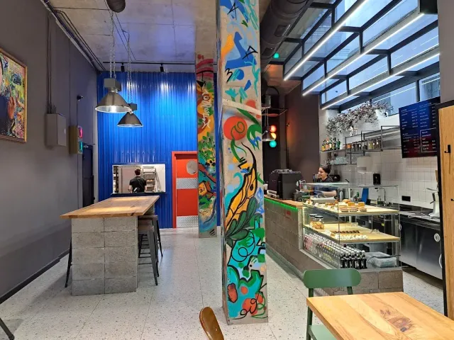 עמוד מצויר בצבעים עזים לצד דלפק מאפים ומנורות תלויות מעל בר עץ