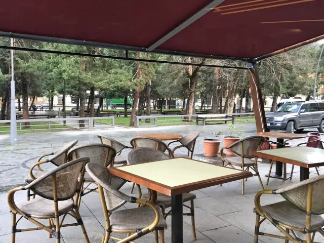 טרסה מקורה עם כיסאות קש ושולחנות, ומאחוריה עצי אורן וכביש