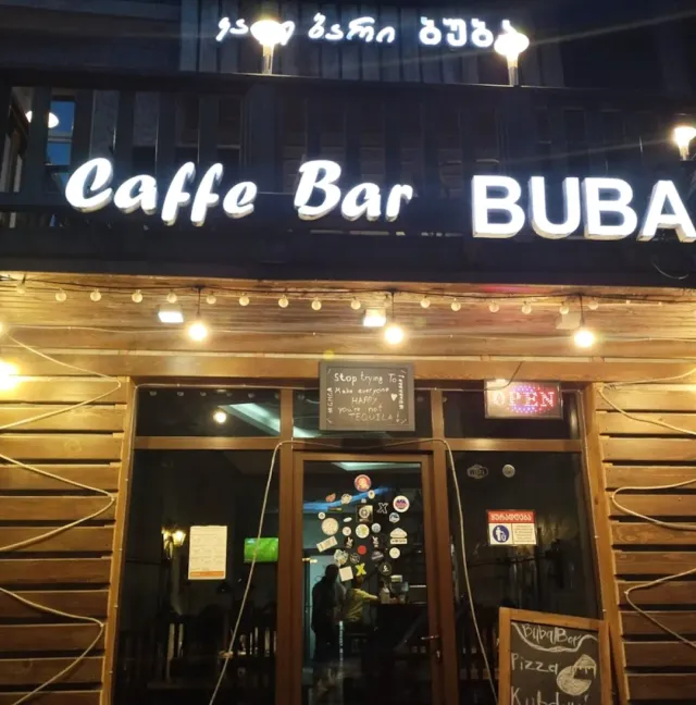 חזית עץ בלילה עם שלט מואר, שרשרת נורות וכניסת זכוכית מכוסה מדבקות