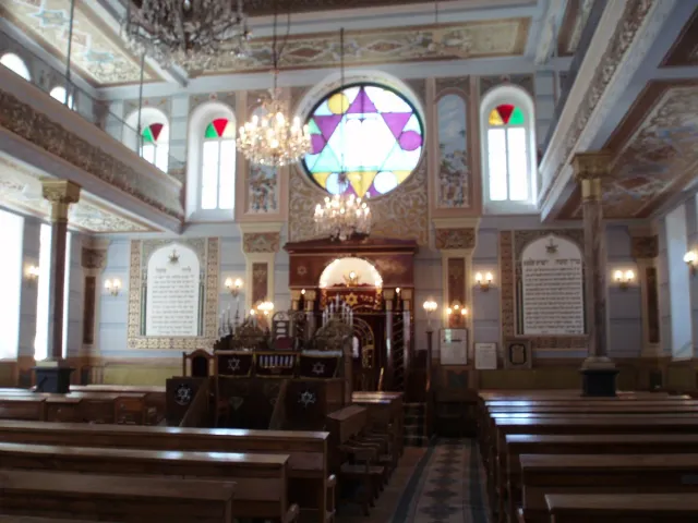 אולם תפילה עם ספסלי עץ, נברשת מרכזית וחלון ויטראז׳ בצורת מגן דוד