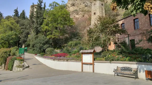 שביל מרוצף עם ערוגות פרחים וספסל, ומעליו חומת אבן על מצוק