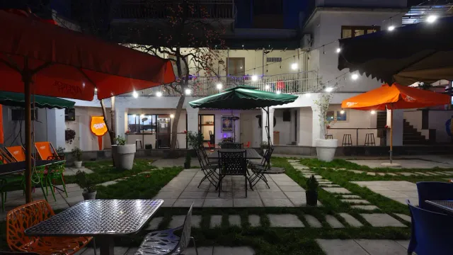 חצר בלילה עם שמשיות כתומות וירוקה, שרשרות נורות ורצועות דשא בין מרצפות