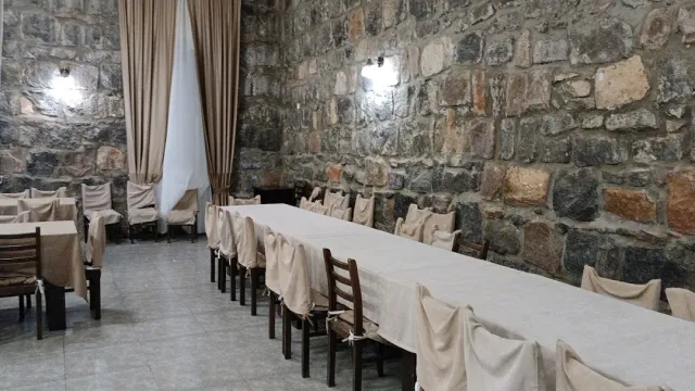 אולם עם קיר אבן גס, שולחן ארוך במפה בהירה וכיסאות בכיסויי בד