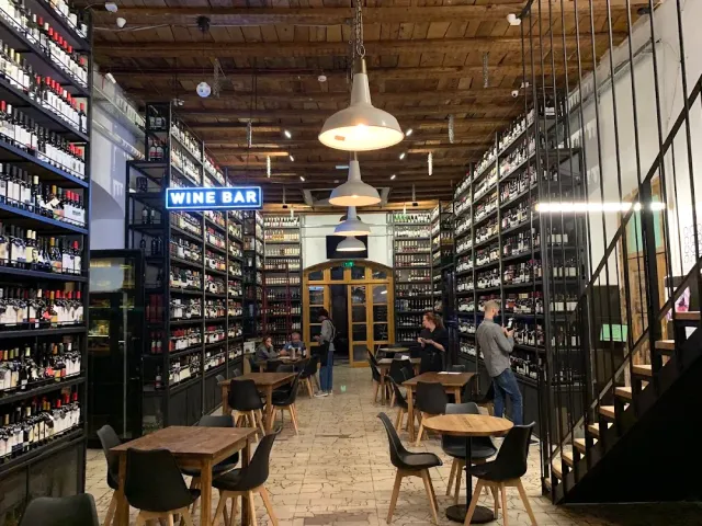 מעבר בין מדפי יין גבוהים משני הצדדים, עם שולחנות עגולים ותקרת עץ