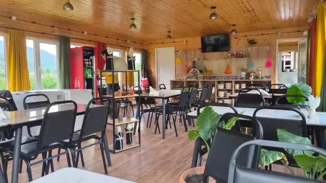 חדר בתקרת עץ עם כיסאות שחורים, וילונות ירוקים וצהובים ודלפק כלים