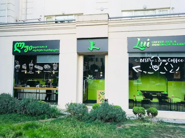 חזית בית קפה עם שתי חזיתות זכוכית גדולות, שילוט ירוק ודשא לפנים