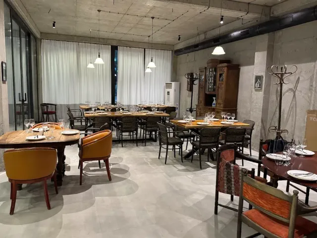 חדר בתקרת בטון עם וילונות בהירים, שולחנות ערוכים, כורסאות חרדל ומזנון עץ