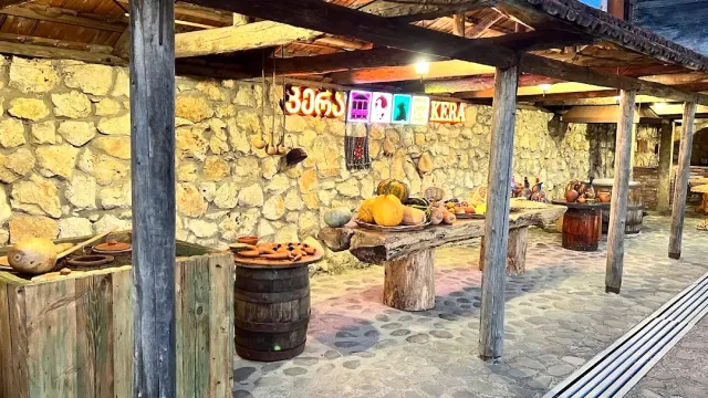 מרפסת אבן מקורה עם עמודי עץ, חביות, כלי חרס ודלעות על שולחן