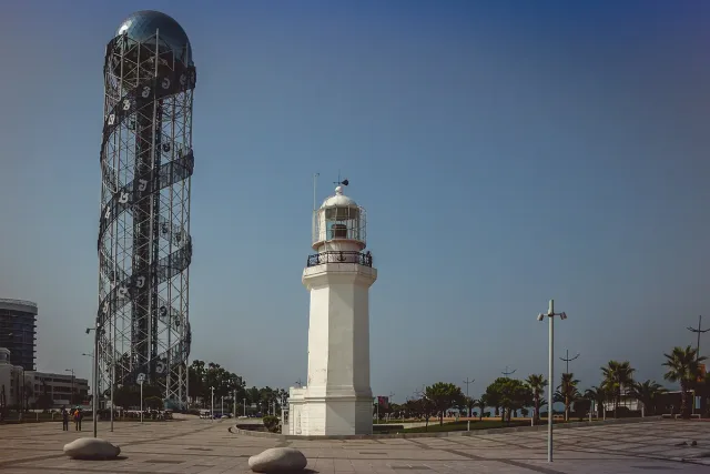 מגדל גבוה עטוף סליל אותיות לצד מגדלור לבן על הטיילת