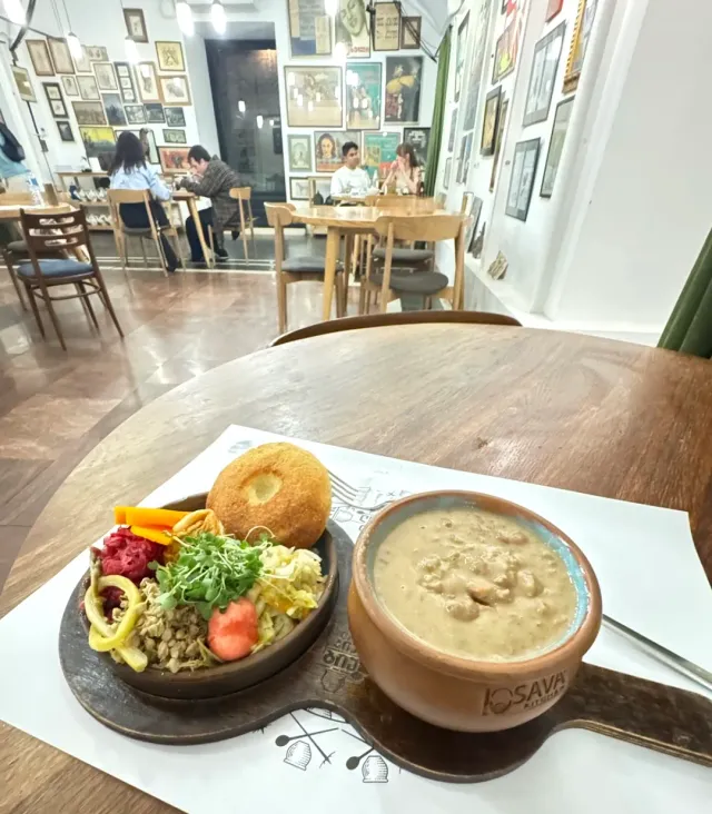 קדרת חרס עם תבשיל שעועית וצלחת מלווים, על רקע קיר תמונות ממוסגרות