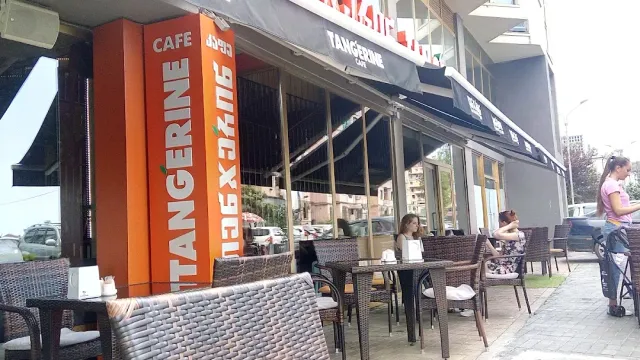 טרסת רחוב עם כיסאות קש, שלט כתום גבוה וסועדים ליד השולחנות