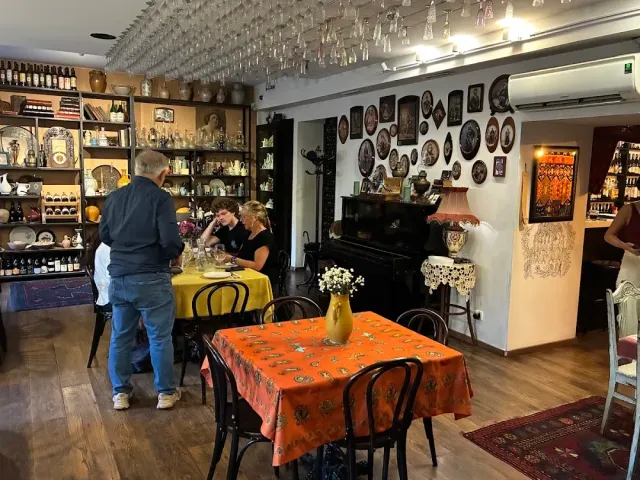 חלל עם מדפי בקבוקים, כוסות תלויות מהתקרה, קיר צלחות ופסנתר שחור