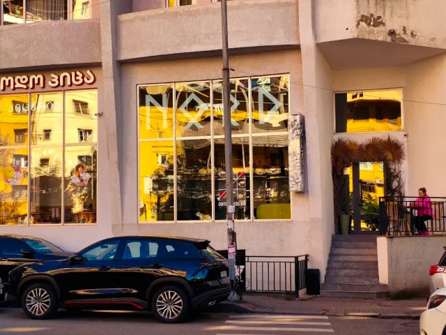 חזית בניין עם חלונות גדולים בזוהר שקיעה, מכוניות חונות ומדרגות בצד
