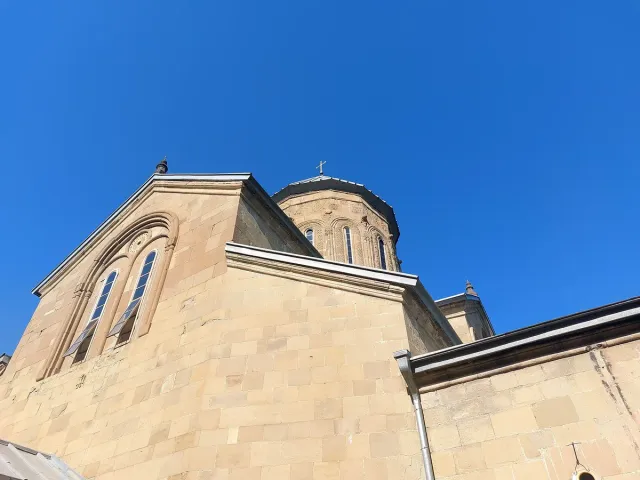 חזית אבן של כנסייה עם חלונות מקושתים וכיפה מאחור מתחת לשמיים כחולים