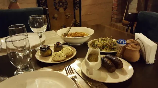 שולחן עם קערת תבשיל, ירקות ממולאים, סלט, נקניקיות ברוטב וכד חרס