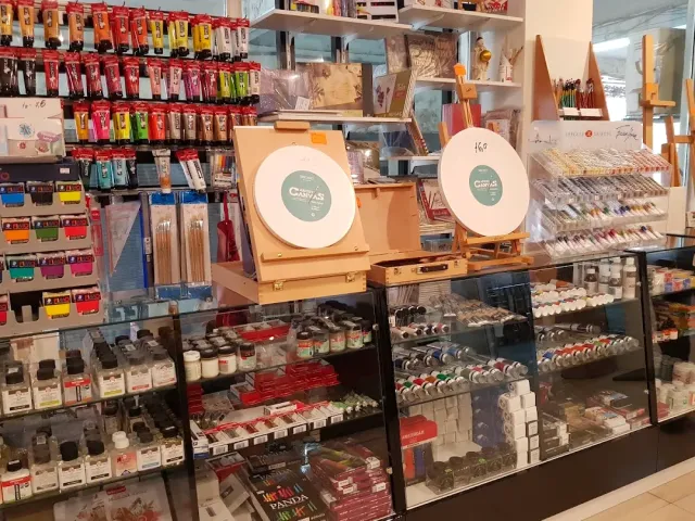 מדפי חנות עם צבעים, מכחולים, עפרונות וכני ציור קטנים בוויטרינה