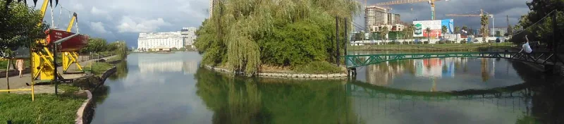 אי קטן עם עצי ערבה בתוך אגם ארדגני בבאטומי, ומגדלי העיר מבצבצים מאחור