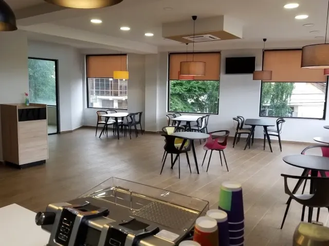 אולם בהיר עם שולחנות וכיסאות ריקים, וילונות כתומים ודלפק עם כוסות צבעוניות