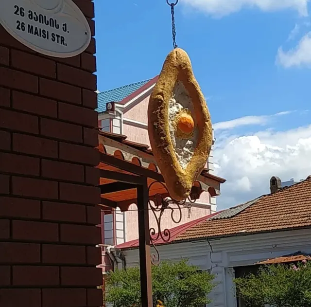 שלט תלוי בצורת לחם סירה עם חלמון, מול בתים ושמי תכלת