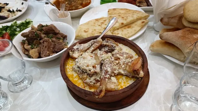 קדרת חרס עם עוף ברוטב לבן, לצד תבשיל בשר, לחמים שטוחים וסלט
