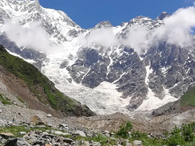 פסגות מושלגות עטויות עננים מעל לשון קרחון וסלעים פזורים בחזית