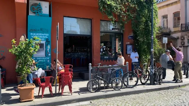 חזית כתומה עם כיסאות אדומים על המדרכה, אופניים חונים ועוברי אורח