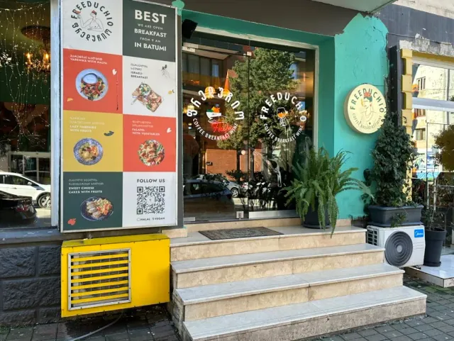 שלט תפריט מאויר ליד חזית טורקיז עם מדרגות אבן, עציצים וחלון ראווה